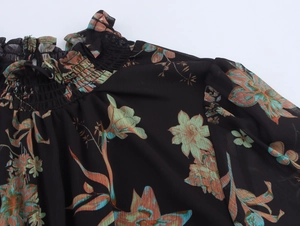 Detail des gesmokten Stehkragens am schwarzen Chiffonkleid mit Blumenmuster und Rüschen
