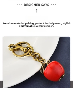 Detail of a red apple keychain with vintage brass chain and leaf accent on white ceramic