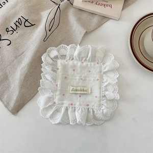 Close-up of white fabric coaster with lace trim, pink hearts, and Sozakka woven label