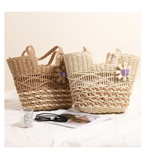 Close-up of woven hollow-out straw bag with decorative flower and butterfly charm