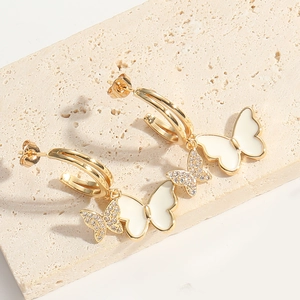 Detail of golden bow earring with white enamel wings and sparkling zircon on a stone