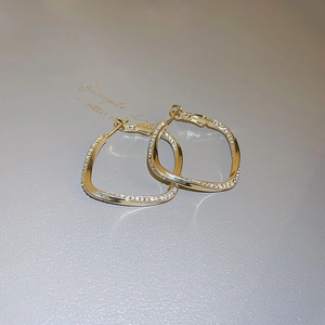 Macro shot of gold geometric earrings with twisted diamond inlay design for women