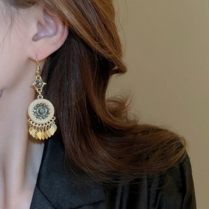 Close-up of bohemian gold leaf tassel earrings with green stone and white pearls on model