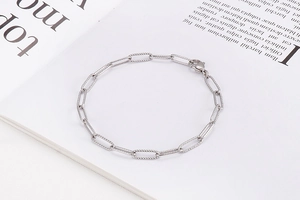 Detail of silver rectangle link bracelet with textured finish and lobster clasp on book