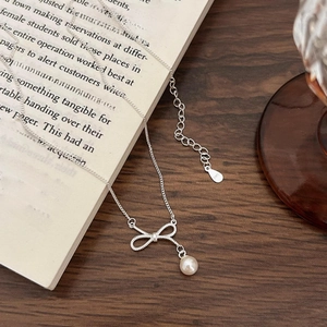 Elegant S925 sterling silver bow pearl necklace displayed on a wooden desk and book