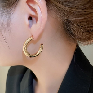 Close-up of golden C-shaped hoop earrings with a textured hammered finish on a model