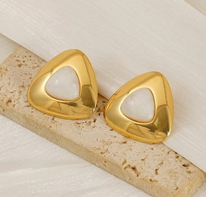 Macro shot of 18K gold-plated triangular earrings with white stone inlay on stone texture
