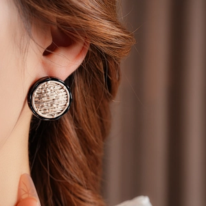 Close-up of minimalist round earring in black and gold on model, showing detailed texture