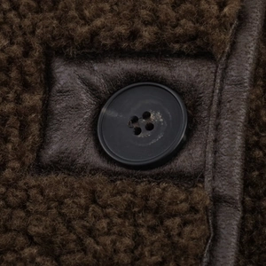Detail of a brown shearling coat featuring a black button and leather reinforcement patch