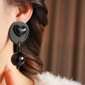 Close-up of a black acrylic heart stud earring with tiered bead tassels on a model