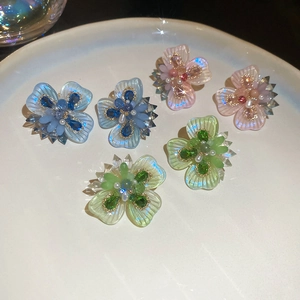 Macro shot of 3D crystal flower stud earrings in blue, pink, and green on a white plate
