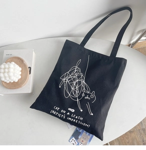 Detail of a black canvas tote bag featuring minimalist white cat line art and task lettering