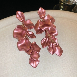 Detail view of mauve pink petal earrings with golden chains on a textured white plate