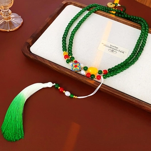 Gros plan détaillé d'un collier en perles de jade vert avec long pompon dégradé et trèfle