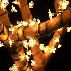 Close-up of warm yellow LED cherry blossom fairy lights wrapped around a tree trunk at night