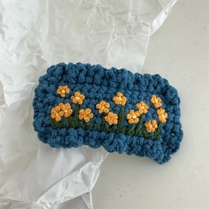 Detail of hand-crocheted blue hair clip featuring yellow flower embroidery on white paper