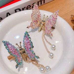 Golden butterfly hair clips with colorful crystals and pearl tassels in a ceramic tray