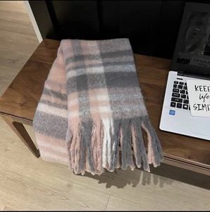Close-up detail of soft pink and grey plaid scarf texture with long tassels on wooden chair