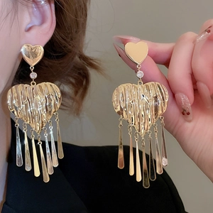 Detail of large gold heart tassel earrings with pleated texture worn by model