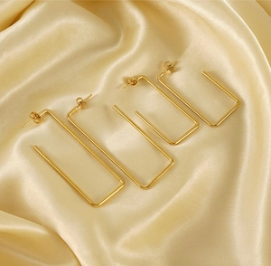 Detail of two pairs of 18K gold-plated stainless steel rectangular earrings on silk