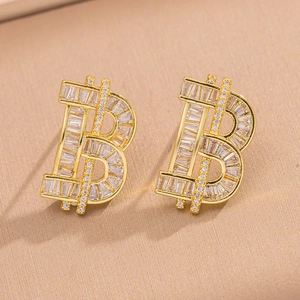 Sparkling gold Bitcoin symbol stud earrings with clear crystals on beige fabric