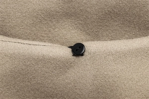Detail of a black round button on a khaki wool-blend jacket with fine stitching texture