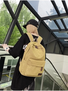 Detail view of khaki canvas backpack with brown leather accents on a model