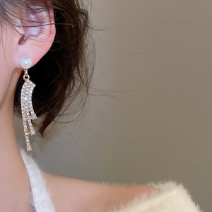 Close-up of elegant gold tassel earrings with pearl and rhinestones worn by a model