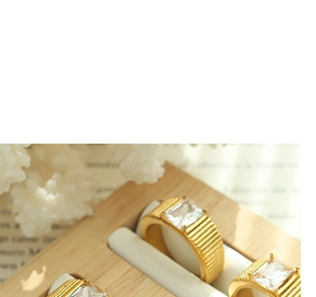 Detail of gold wide band rings with square stones and ribbed texture in a wooden box