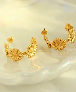 Detailed close-up of C-shaped matte gold sunflower earrings on a pearlescent tray
