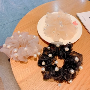Three organza scrunchies with pearls in cream, mauve, and black on a wooden table