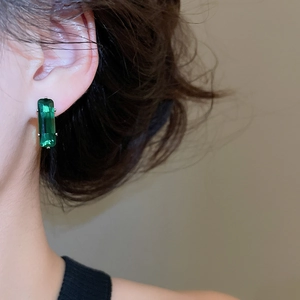 Close-up of elegant emerald green rectangular zircon stud earring worn on ear lobe