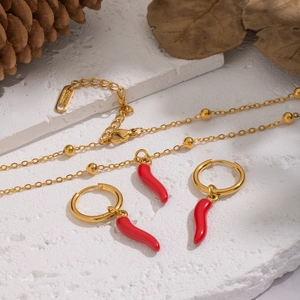 Close-up of golden stainless steel necklace and earrings set with red chili pendants
