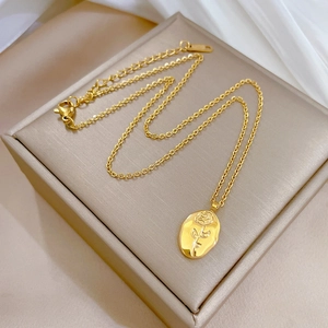 Detail view of a rose embossed gold pendant necklace on a premium metallic jewelry box