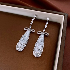 Detail of silver drop earrings with zircon bow and white resin teardrop charms