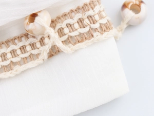 Close-up of white cotton-linen fabric with khaki crochet fringe and shell bead details