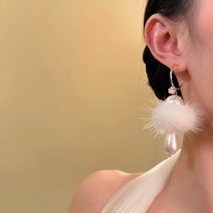 Detail view of gold C-shape drop earring with white fur ball and large teardrop pearl