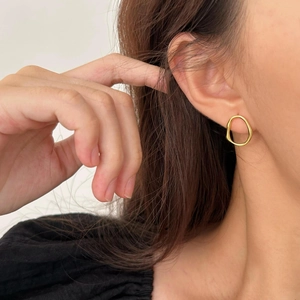 Close-up of golden irregular geometric hoop earring worn by a model in minimalist style
