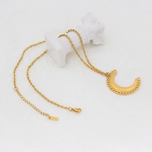 Collier croissant de lune doré avec texture fine sur un support en pierre minimaliste