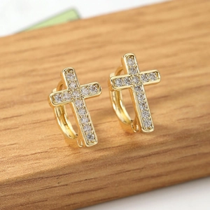 Elegant gold cross drop earrings featuring pavé cubic zirconia on a warm wooden surface