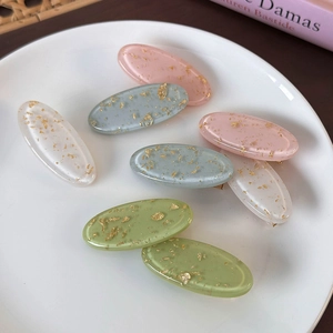 Flat lay of oval resin hair clips with gold foil flakes on a white plate