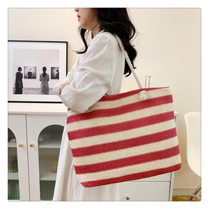 Fashionable large woven tote bag with red and beige stripes shown on female shoulder