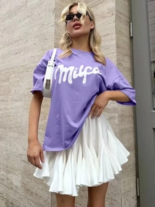 Λεπτομέρεια από μωβ βαμβακερό t-shirt με λευκή πλισέ φούστα και τύπωμα Milpa σε στυλ δρόμου