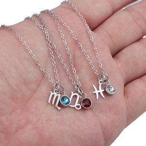 Three stainless steel zodiac necklaces with birthstones held by hand in a high-detail shot