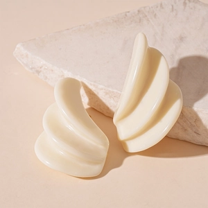 Detail view of cream resin geometric triple layer stud earrings on a textured stone