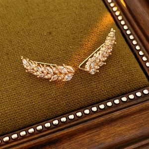 Close-up of golden leaf earrings with shimmering zircons and delicate small pearls