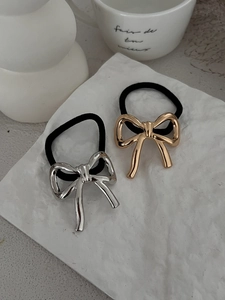 Detail of gold and silver polished metal bow hair ties on minimalist textured card