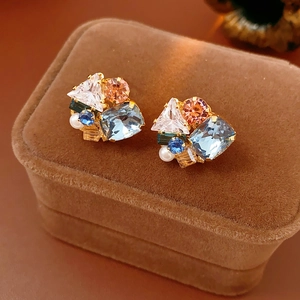 Detailed macro view of gold-tone earrings with multi-color zircons and white pearl on velvet