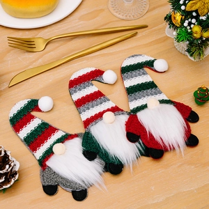 Three Christmas gnome cutlery holders with striped knit hats on a rustic wooden table