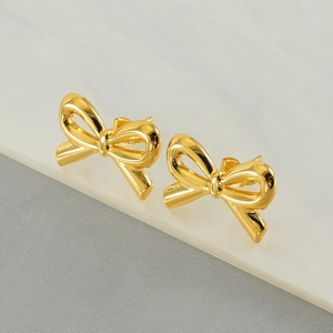 Elegant polished golden stainless steel bow stud earrings on marble and fabric background